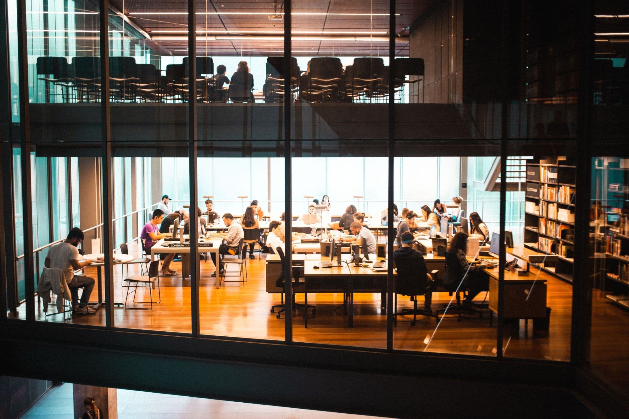 People working at desks in a bright open-plan workspace, seen through a glass facade