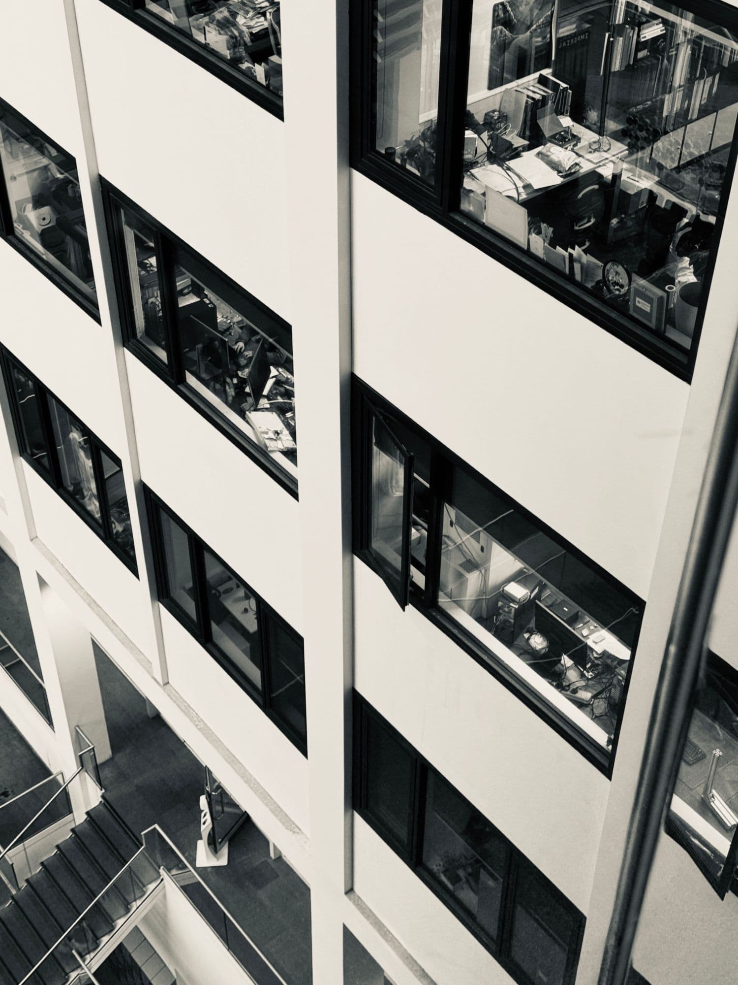 Office windows in a multi-storey atrium, with desks, screens and papers visible inside